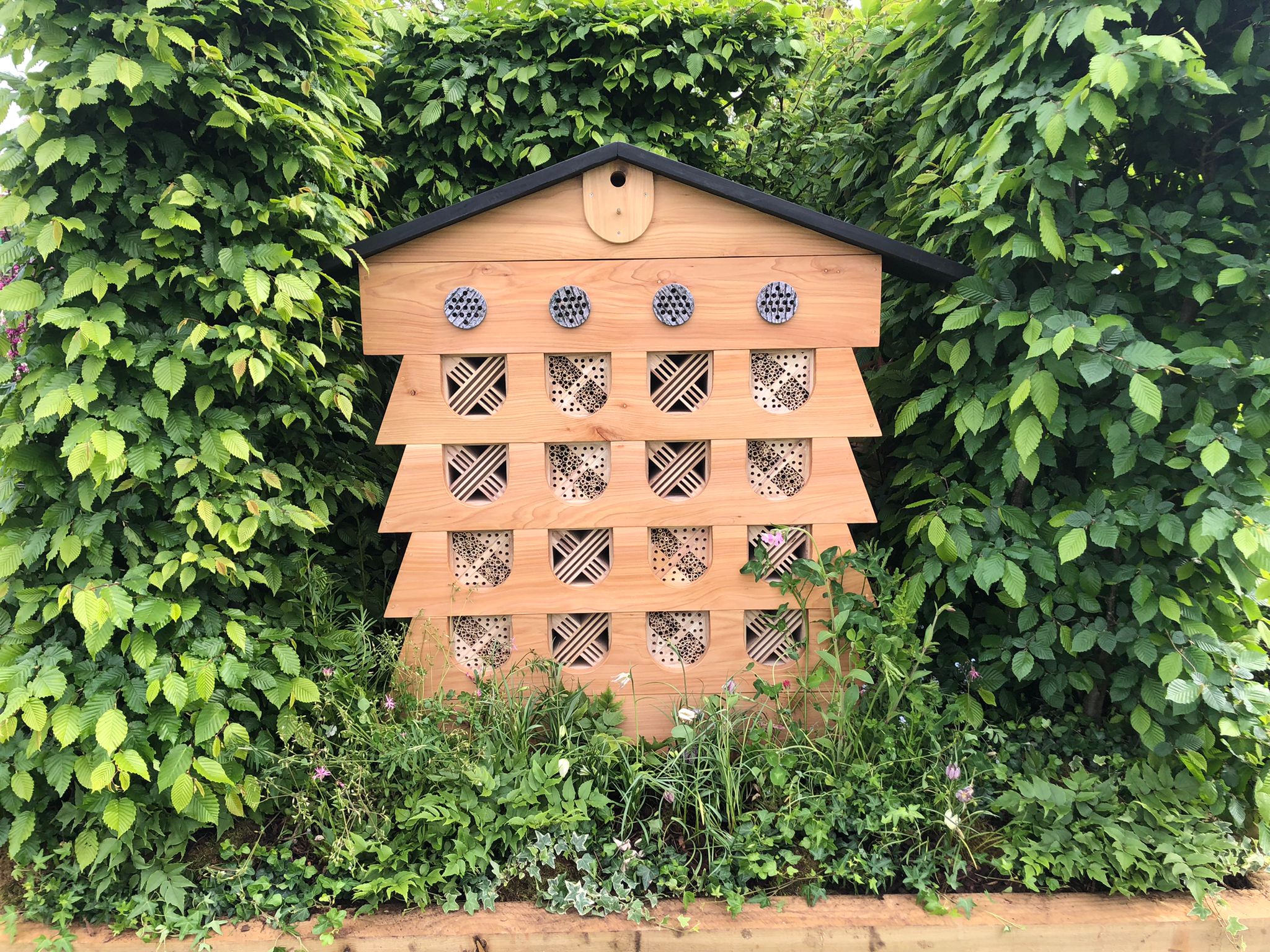 A large wooden insect hotel for wildlife amongst some bushes as Gardeners' World Spring Fair.